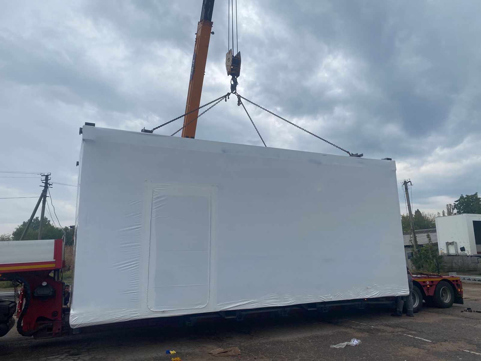 A modular industrial unit being lifted by crane onto a low-bed trailer for relocation in Ukraine